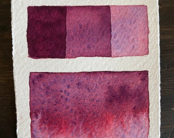 May include: A rectangular piece of textured white paper featuring a watercolor swatch labeled Ultram. Purple. The top section displays three squares in varying shades of purple, while the bottom section shows a larger rectangular wash of purple.