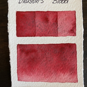 Peut inclure: Une carte d'échantillons de peinture aquarelle avec le texte "Dragon's Blood" en haut. La carte montre trois nuances différentes de peinture rouge, d'un rouge foncé à un rose plus clair.