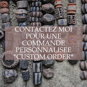 Può includere: Perline artigianali di varie forme e colori, tra cui marrone, grigio e blu, disposte su una superficie sabbiosa. L'immagine include il testo: "CONTACTEZ MOI POUR UNE COMMANDE PERSONNALISEE *CUSTOM ORDER*."