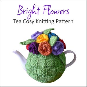 Könnte beinhalten: Eine grüne gestrickte Teekanne mit einem bunten Blumendesign. Die Teekanne ist in Form einer Teekanne geformt und hat ein gewebtes Muster. Die Blumen sind aus Garn in den Farben Lila, Orange, Gelb und Rot.