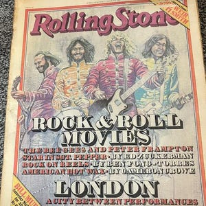 May include: Vintage Rolling Stone magazine cover featuring a group of musicians with guitars and drums. The cover has the text "ROCK & ROLL MOVIES" and "LONDON". The magazine is aged with a red and pink border.