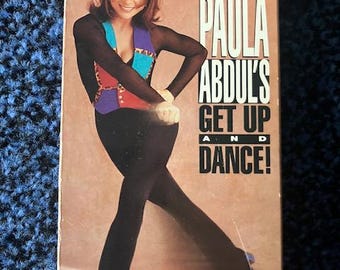 May include: A VHS tape cover featuring Paula Abdul in a black and red workout outfit, with the title "Paula Abdul's Get Up and Dance! An Aerobic Dance Workout"