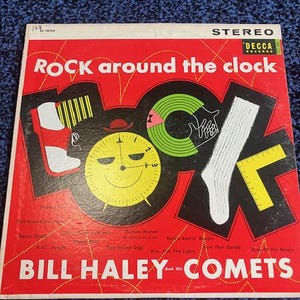 Peut inclure: Pochette d'album vinyle vintage pour "Rock Around the Clock" de Bill Haley and His Comets. La couverture est rouge avec des éléments graphiques noirs et jaunes, dont un cadran d'horloge et une chaussette. Le titre de l'album et le nom de l'artiste sont en blanc.