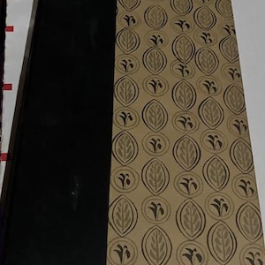 May include: A hardcover book with a black spine and a tan cover with a repeating pattern of stylized leaves and flowers.