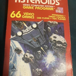 May include: A retro Asteroids video game box. The red box has the game title in white and yellow, with the Atari logo. The box art shows a spaceship in space, avoiding asteroids. The box reads "66 Video Games".