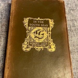 Pu&ograve; includere: Un libro rilegato in pelle marrone con lettere dorate sulla copertina. Il titolo &egrave; "Nei mari del sud" di Robert Louis Stevenson.