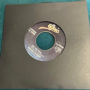 May include: A black 45 RPM vinyl record in a black sleeve. The record label is black and gold with the text "OFF THE WALL" and "MICHAEL JACKSON". The record is from the album "OFF THE WALL".