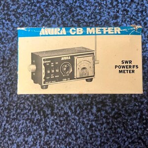 May include: An Akira CB meter in its original box. The box is white with blue accents and text. The meter is black with a silver dial and various knobs and switches. The text on the box reads "SWR POWER/FS METER".