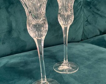 May include: Two clear glass candle holders with a textured design. The candle holders have a tall, slender stem and a wide base.