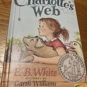 May include: A hardcover copy of "Charlotte's Web" by E.B. White, with illustrations by Garth Williams. The cover art features a young girl with a pig and a goose, with the title in large, stylized letters.
