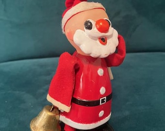 May include: A vintage Santa Claus figurine with a red suit, white beard, and a red hat. The figurine has a gold bell in one hand and black shoes. The Santa Claus figurine is a classic Christmas decoration.