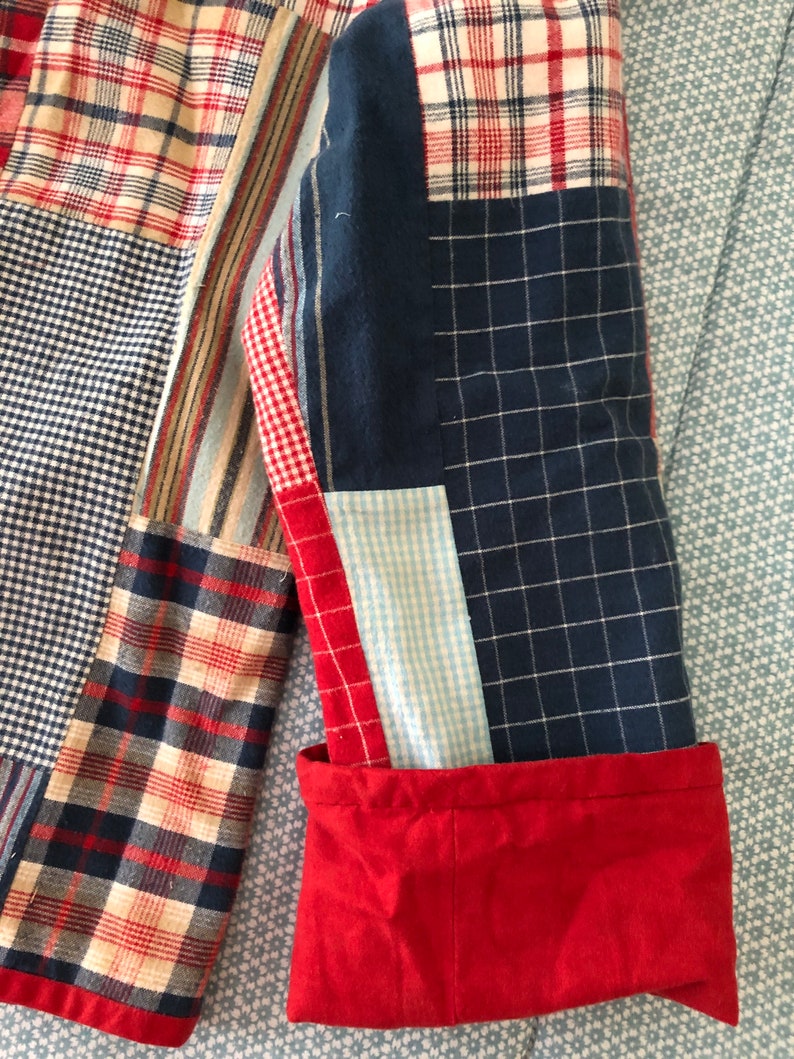 Peut inclure: Une veste &agrave; manches longues compos&eacute;e d'un patchwork de tissus vari&eacute;s, incluant des motifs &agrave; carreaux rouges, blancs et bleus, des quadrillages bleu marine et des vichys bleu clair. La manche pr&eacute;sente un poignet rouge uni contrastant.
