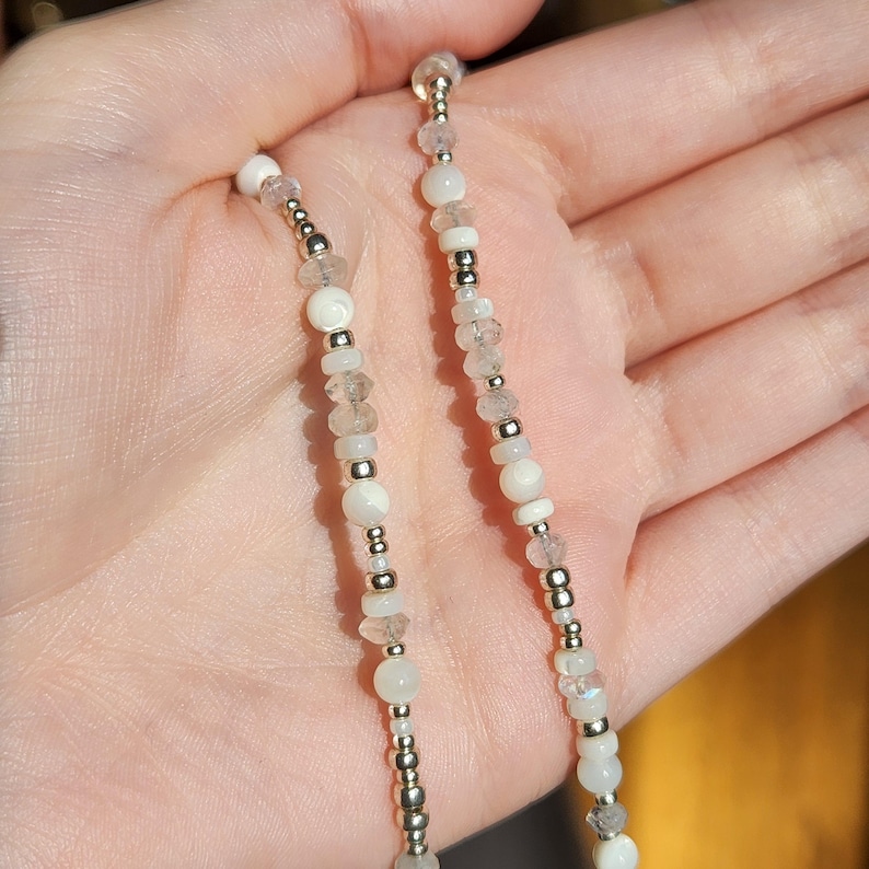 May include: A white and gold beaded necklace with white and clear round beads. The necklace is made of small, delicate beads and is perfect for layering.