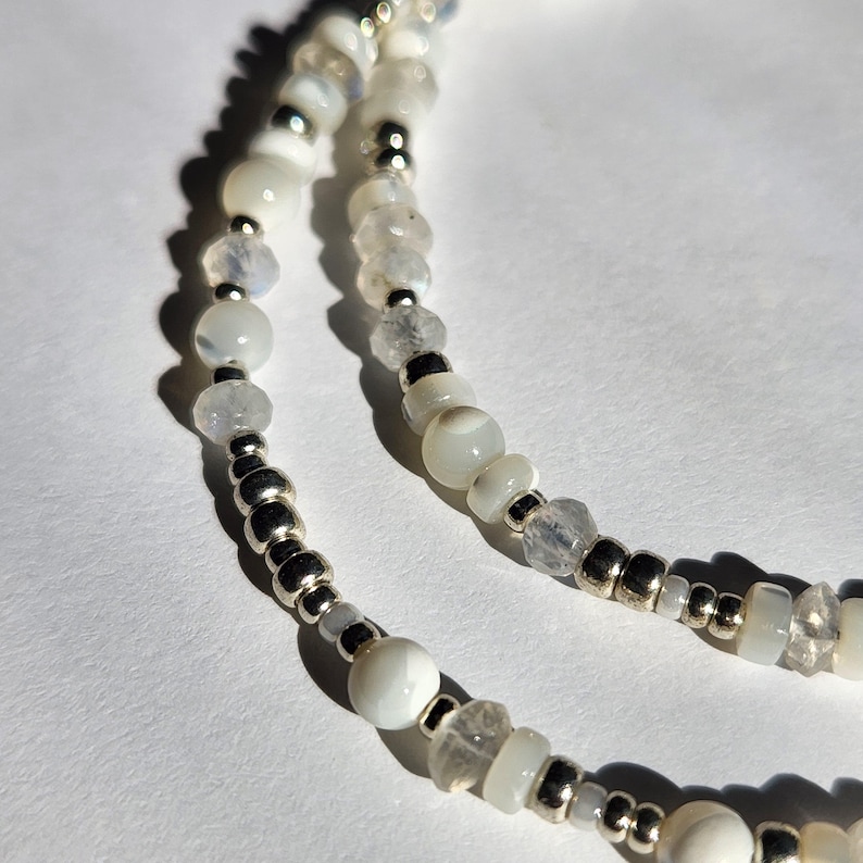 May include: A white beaded necklace with silver beads and moonstone beads.
