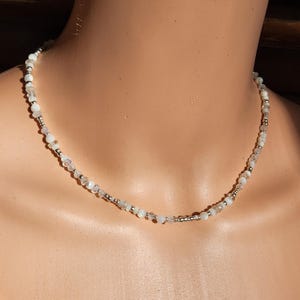 May include: A delicate silver necklace with white and iridescent beads. The necklace is made of small, round beads that are strung together on a silver chain.