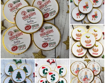 Op de afbeelding: Assortiment van ronde chocolade-favorieten met verschillende kerstthema's. Sommige hebben een rendier, een kerstpudding, een kerstboom en een Peter Rabbit-ontwerp. Andere hebben gepersonaliseerde namen zoals "Sofia", "Stuart", "Oliver", "Chloe", "Sofia", "Harry" en "Mummy".