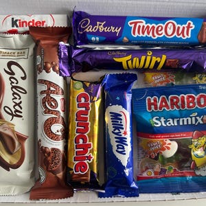 May include: A box filled with various chocolate bars and candies. Brands include Kinder, Galaxy, Aero, Crunchie, Milky Way, Cadbury Time Out, Twirl, and Haribo Starmix. The packaging features a variety of colors and text.