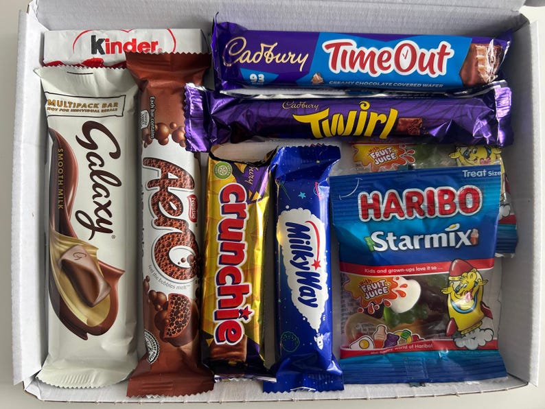 May include: A box filled with various chocolate bars and candies. Brands include Kinder, Galaxy, Aero, Crunchie, Milky Way, Cadbury Time Out, Twirl, and Haribo Starmix. The packaging features a variety of colors and text.