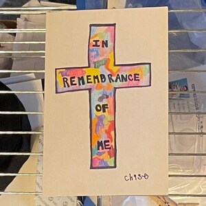 May include: A hand-drawn cross with the words "IN REMEMBRANCE OF ME" in black lettering. The cross is filled with colorful abstract shapes. The artwork is signed "ch19-o".