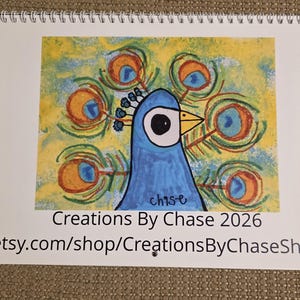 May include: A spiral-bound notepad featuring a colorful peacock illustration. The peacock is blue with a large eye and a yellow beak, surrounded by orange and blue feather details. The notepad includes the text "Creations By Chase 2026" and a shop URL.