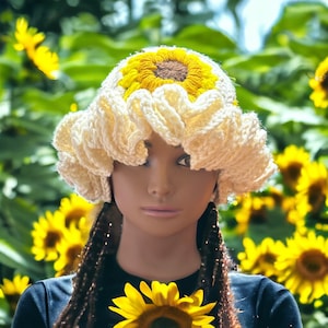 May include: A crocheted sunflower hat with a white base and yellow petals. The hat has a brown center with a yellow circle in the middle. The hat is worn by a mannequin with long brown braids.