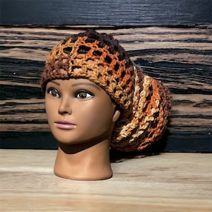 May include: A crocheted hair bonnet in brown, orange, and cream colors. The bonnet is made with a loose, open weave and has a gathered look.