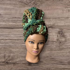 May include: A green, brown, and beige crocheted head wrap. The wrap is tied in a knot on top of the head.