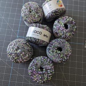 May include: Six round balls of yarn featuring a metallic silver mesh structure interwoven with small, multicolored rectangular flecks in shades of green, pink, and blue. Each ball has a white paper label with the text GIOCO 6420 printed on it.