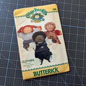 May include: Vintage Butterick sewing pattern for Cabbage Patch Kids clothes. The yellow and white pattern cover features illustrations of three Cabbage Patch Kids dolls. The text on the cover reads "CLOTHES For your Cabbage Patch Kids!" and "BUTTERICK".