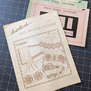 May include: Three vintage paper booklets featuring huck weaving and towel patterns. The top booklet is light green, the middle is pink, and the front booklet is cream with brown illustrations of various textile designs and the text Aunt Martha's.