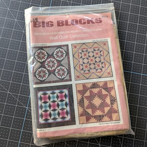 May include: A package of tissue paper foundations for piecing wall quilt patterns. The package features four quilt block designs, including "GOG Fellow's Star" and "Delectable Mountains." The package is sealed in a clear plastic bag and rests on a black cutting mat.