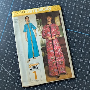 May include: A vintage Simplicity sewing pattern, size 8-10 Miss, featuring illustrations of two long dresses. The pattern cover has the text "5740 Simplicity" and "Super Jiffy easy cut easy sew". The background is a black cutting mat.