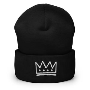 May include: Black beanie with a white embroidered crown design. The crown has three dots in the center.