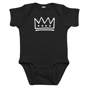 May include: Black baby bodysuit with a white crown graphic. The crown design features a series of peaks and three small circles. The bodysuit is made of soft fabric and has short sleeves.