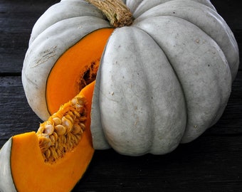 Puede incluir: Una calabaza gris con un interior naranja claro está cortada por la mitad y se ha quitado una rebanada. La calabaza está sobre una superficie negra.