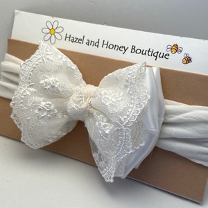 Puede incluir: Diadema de encaje blanco con una banda el&aacute;stica blanca. La diadema est&aacute; sobre una tarjeta marr&oacute;n con el texto "Hazel and Honey Boutique" y una margarita.
