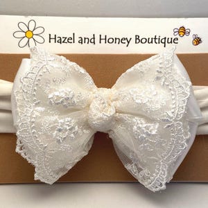 Puede incluir: Diadema de encaje blanco con una banda el&aacute;stica blanca. La diadema est&aacute; sobre un fondo marr&oacute;n con el texto "Hazel and Honey Boutique".