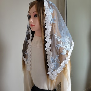 May include: A light blue and white floral lace veil. The veil is draped over a mannequin head, showcasing its delicate design. The edges are trimmed with white floral lace, and the veil features light blue floral embroidery.