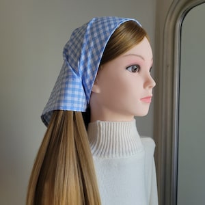 Puede incluir: Un pañuelo a cuadros azul claro y blanco con textura de lunares se muestra en un maniquí. El pañuelo está atado en la parte posterior de la cabeza. El maniquí lleva un jersey de cuello alto blanco. Un accesorio clásico.