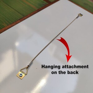 May include: A white framed picture with a hanging attachment on the back. The attachment is a small triangular metal piece with a screw and a wire.