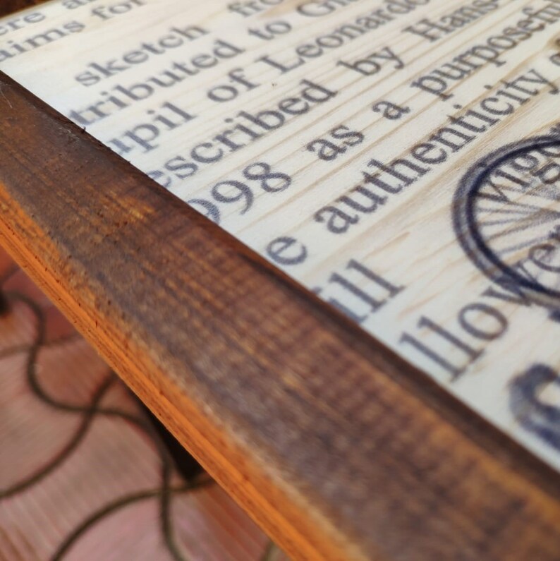 May include: A close-up of a wooden frame with a printed text inside. The text reads "cre aims for sketch f tributed to upil of Leonard escribed by Han 98 as a purposefu e authenticity 111 llowe".