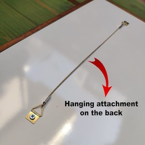 May include: A white framed picture with a hanging attachment on the back. The attachment is a small triangular metal piece with a screw and a wire.