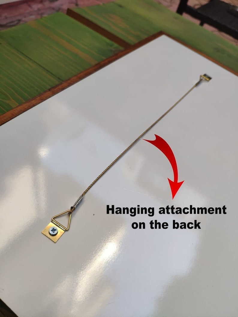 May include: A white framed picture with a hanging attachment on the back. The attachment is a small triangular metal piece with a screw and a wire.