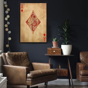 May include: A framed print of the Ace of Diamonds playing card with a red and gold design on a textured background. The card is framed in black and hangs on a dark blue wall.