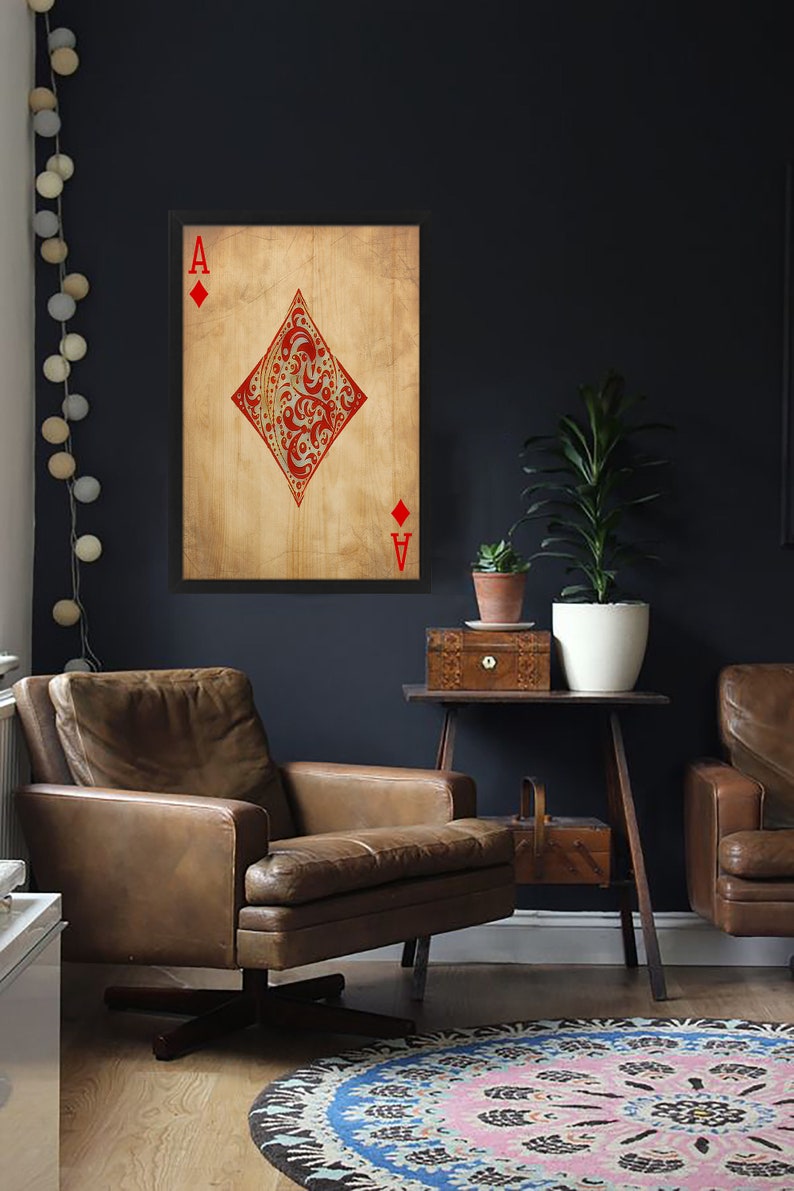 May include: A framed print of the Ace of Diamonds playing card with a red and gold design on a textured background. The card is framed in black and hangs on a dark blue wall.