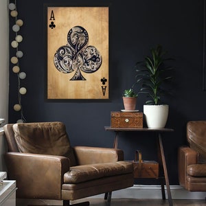 May include: A vintage-style illustration of the Ace of Clubs playing card. The card is framed and hanging on a dark blue wall. The card features a detailed, ornate design of a clover with swirls and flourishes. The card is surrounded by a brown background.