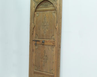 May include: A carved wooden door with an arched top and intricate details. The door is made of light brown wood and has a dark brown metal handle.