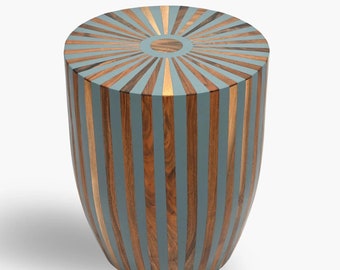 May include: A round wooden stool with a blue and brown striped design. The top of the stool has a sunburst pattern with a circle in the center.