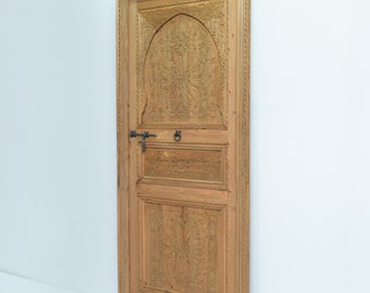 May include: A carved wooden door with a traditional Moroccan design. The door is made of light brown wood and has a decorative arch at the top. The door is also decorated with intricate carvings of flowers and geometric patterns.