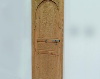 May include: A carved wooden door with an arched top and intricate geometric patterns. The door is made of light brown wood and has a dark metal latch.